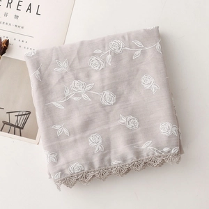 Détail de broderies roses blanches et dentelle au crochet sur une écharpe en coton et lin