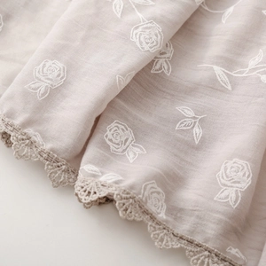 Détail d'une écharpe en coton et lin avec broderie de roses et bordure en dentelle