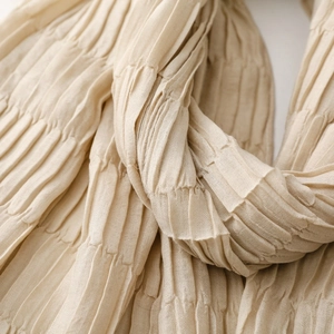 Macro shot of beige pleated scarf fabric texture with detailed vertical creased patterns