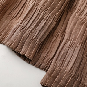 Close-up of brown pleated fabric texture showing vertical micro-crease details and hem