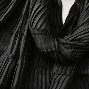 Close-up of black pleated fabric texture with detailed vertical micro-folds and soft shadows