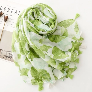 Detail of bohemian scarf with green ginkgo leaf print and fringe tassels on a table