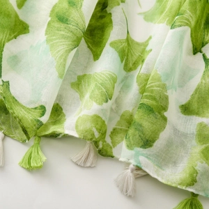 Detail of green ginkgo leaf print scarf with woven fringe tassels and soft linen texture