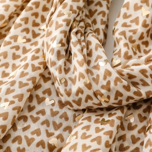 Detail of soft cream scarf featuring brown and gold foil heart prints with fine texture