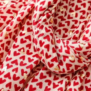 Macro detail of scarf fabric with red and gold heart print on textured beige surface