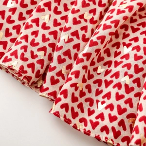 Macro detail of red and gold foil heart prints on cream-colored satin scarf fabric