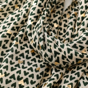 Detail of beige scarf featuring golden foil hearts and dark green heart patterns