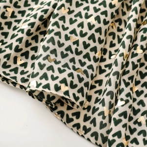 Close-up of beige scarf fabric featuring green flocked and gold foil heart prints