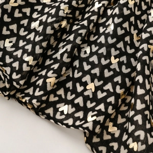 Macro detail of black fabric scarf with metallic gold and white heart prints