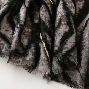 Macro detail of zebra print scarf with gold metallic accents and frayed fringe edges