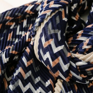 Close-up of pleated scarf showing navy and beige geometric wave patterns and texture