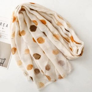Detailed view of cream scarf with orange and brown foil polka dots and frayed edge