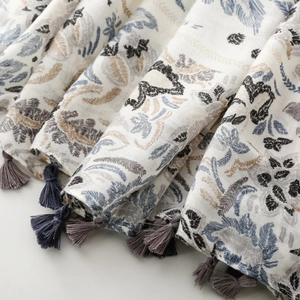 Macro detail of cotton-linen floral scarf showing leaf prints and tassel ornaments