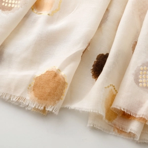 Detail of soft lightweight scarf featuring metallic gold polka dots and fringe edges