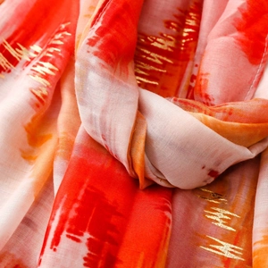 Macro detail of scarf featuring gold foil stripes and artistic orange ink wash pattern