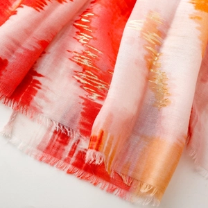 Detail of red and orange gradient scarf with metallic gold foil texture and frayed edges