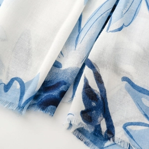 Detail shot of white scarf featuring blue floral prints and delicate frayed edges