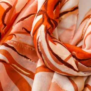 Close-up of lightweight satin scarf with orange abstract patterns and gold foil detail