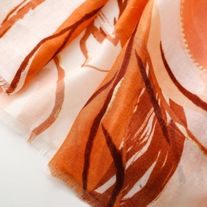 Detailed macro view of orange and white floral silk scarf with golden powder accents