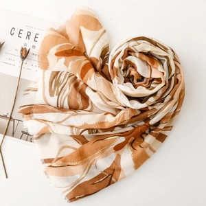 Detail of thin floral scarf with gold foil accents and tassel edges on white background