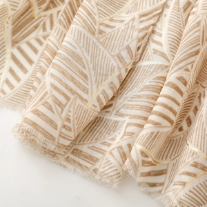 Detailed macro view of beige leaf pattern scarf with gold thread and fringe edges