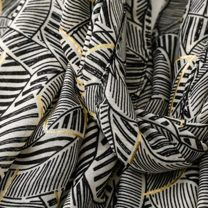 Macro detail of scarf fabric showing black and white leaf patterns with gold foil accents