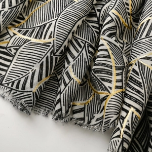 Detailed macro view of satin scarf fabric with gold leaf patterns and fringed edges