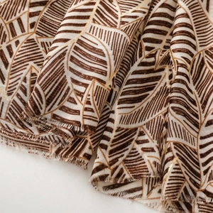 Macro view of scarf featuring gold foil leaf patterns and natural frayed edges texture