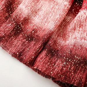 Detail of red and cream gradient fabric with fine pleats and shimmering gold foil speckles