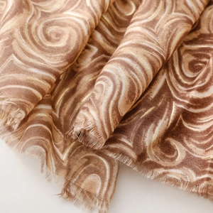 Vue macro d'un foulard doux avec motifs marbrés dorés et finitions à franges naturelles