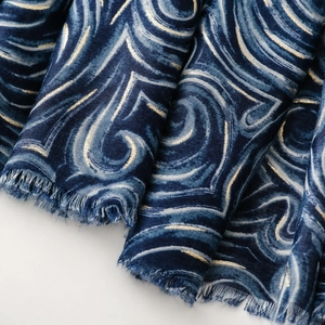 Détail d'une écharpe bleu marine à imprimé latte doré et bordures à franges souples