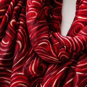 Vue détaillée du tissu en satin rouge foncé avec motifs tourbillonnants dorés et texture soyeuse