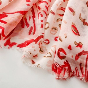 Detail of pink scarf with red lip prints and abstract patterns featuring frayed edges