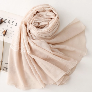 Close-up of light beige scarf featuring delicate white floral embroidery and rolled edges