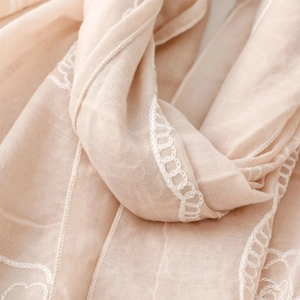 Detail of light beige embroidered shawl featuring intricate white circular patterns and soft texture
