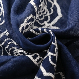Detailed macro view of white floral embroidery on premium navy blue linen scarf fabric