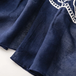 Detail of navy blue lightweight fabric with intricate white ring embroidery on the edge