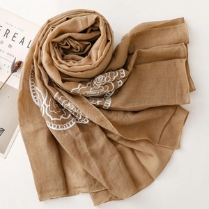 Detail of light brown scarf with white floral embroidery and neat rolled edges