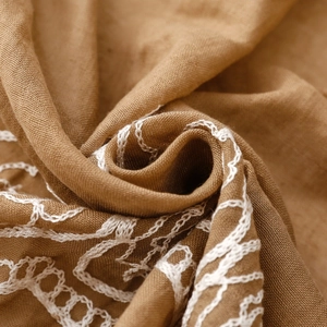 Macro shot of brown ethnic scarf showing intricate white chain embroidery and linen texture