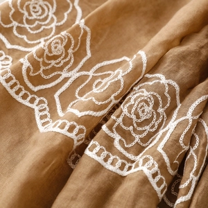 Close-up of white rose embroidery on dark khaki ethnic style textured scarf fabric