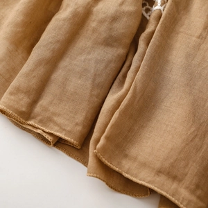 Close-up of brown linen scarf featuring delicate white lace trim and fine hem details