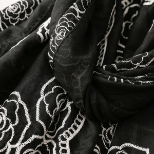 Macro detail of rose flower embroidery on black fabric scarf with fine linen texture