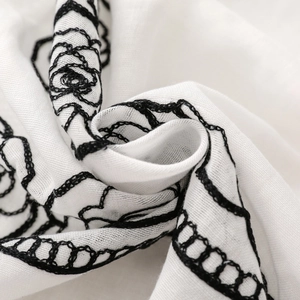 Detailed close-up of ethnic rose embroidery on soft white fabric with fine chain stitching