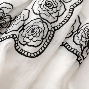 Close-up of black rose floral embroidery on white lightweight shawl fabric texture