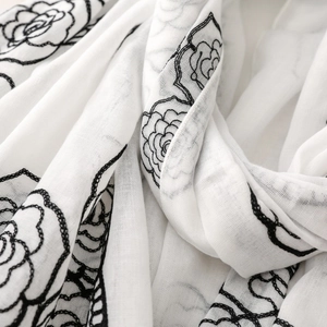 Close-up of black floral embroidery on a soft white cotton scarf showing detailed texture