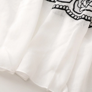 Detail of white cotton linen fabric with black floral embroidery and breathable texture