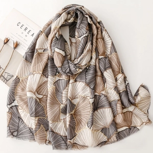 Elegant ginkgo leaf print scarf with gold accents and soft fringe on a neutral base