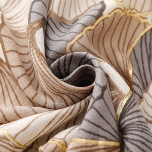 Macro detail of soft cotton-linen scarf featuring golden ginkgo leaf print texture