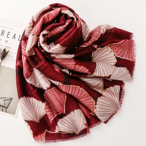 Detail of red and pink scarf featuring golden ginkgo leaf prints and soft fringe edges