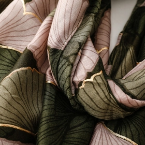 Detail of soft scarf featuring golden ginkgo leaf patterns on silk-like fabric texture